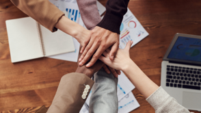 Decorative stock image of six people putting their hands in for a group celebration over a desk